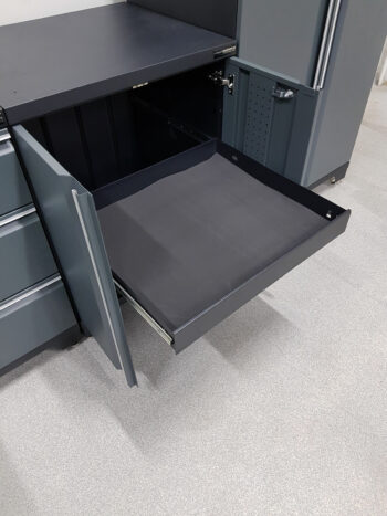 Verktygsskåp med 1 låda och dörrar grå, PRO har en öppen metalllåda med svart foder som sträcker sig från en mörkgrå enhet, mot ljust texturerat golv. Den innehåller ytterligare stängda lådor och ett högt fack.