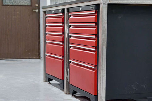 Verktygsskåp i röd metall med flera lådor är snyggt arrangerade under en arbetsbänk i garaget och visar upp den praktiska Garageinredningen. En stängd trädörr står tyst i bakgrunden och fullbordar verkstadsinställningen.