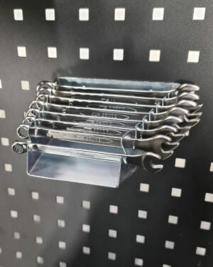 En uppsättning glänsande Ringnyckelhållare liggande metallnycklar organiserade på en grå pinnbräda med små fyrkantiga hål, inriktade i ett ställ, som visar olika storlekar. Belysningen framhäver deras metalliska finish.