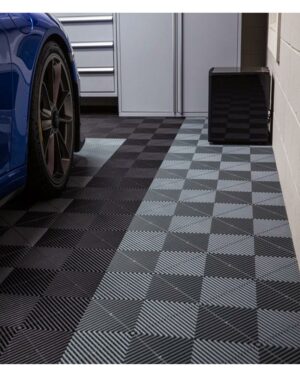 Ett garage med rutigt golv av SWISSTRAX RIBTRAX golvplattor i geometriskt mönster. Ett blått sportbilshjul syns till vänster, parkerat på golvet. Hyllor och ett skåp står i bakgrunden mot en ljus vägg.