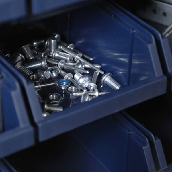 En blå förvaringsbehållare, överfull med diverse metallbultar, skruvar och muttrar, står noggrant organiserad på garageinredningshyllan.
